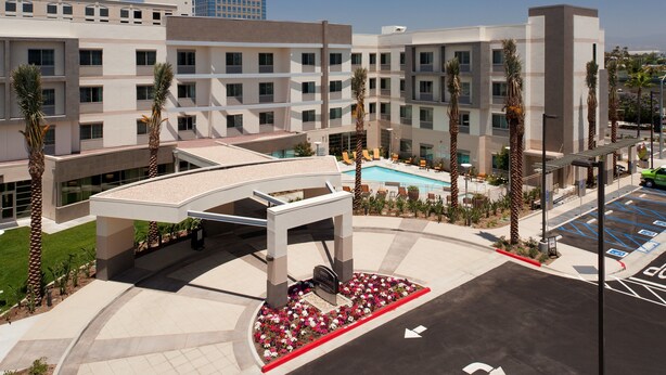 A modern hotel with a pool, palm trees, and a parking area.