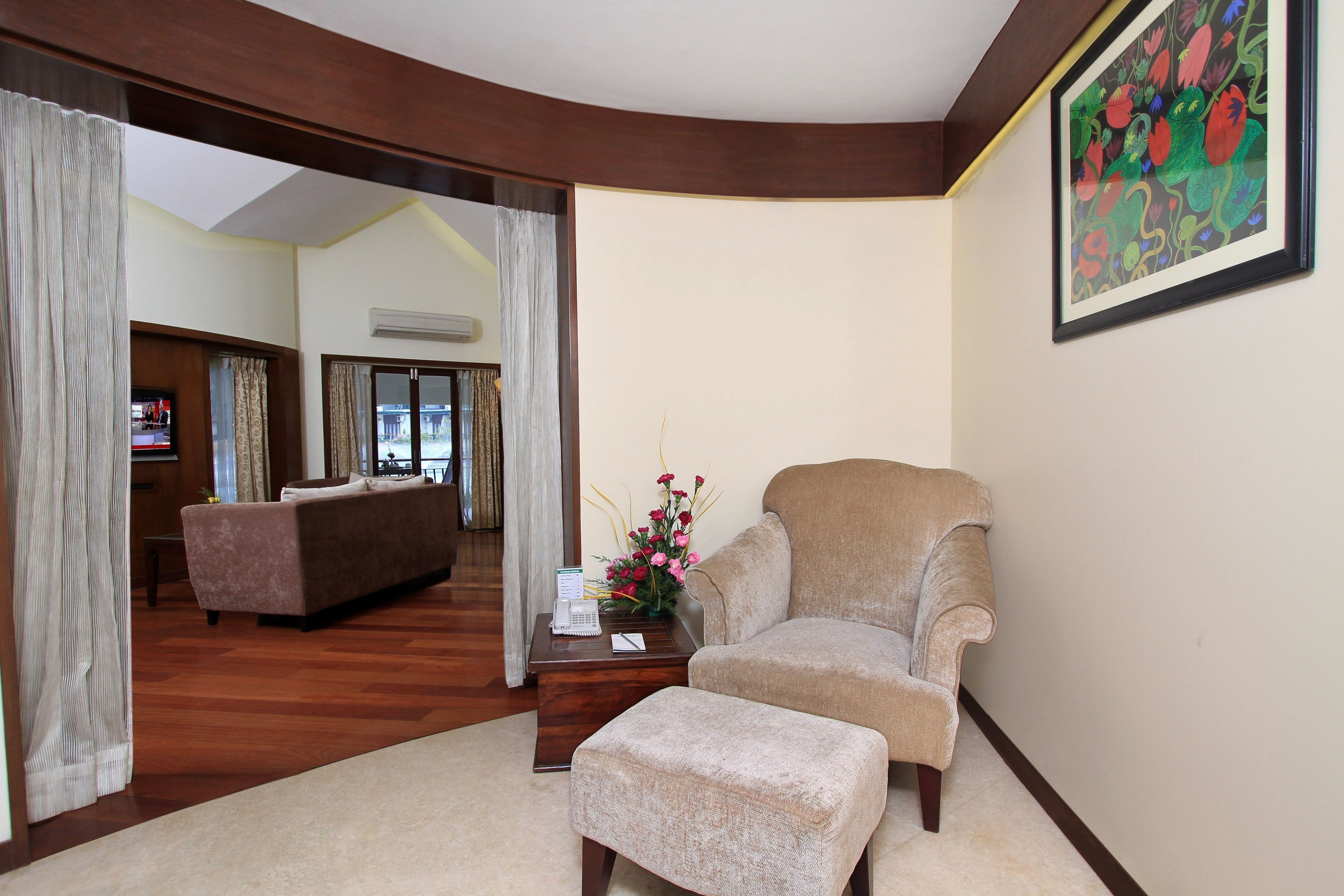 A living room with a sofa, armchair, and ottoman, a coffee table with a vase of flowers, and a painting on the wall.