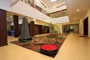 A spacious lobby with a central garden area featuring a large planter with red flowers, a decorative ship, and various plants. - Silent Shores Resort & Spa (Mysore)