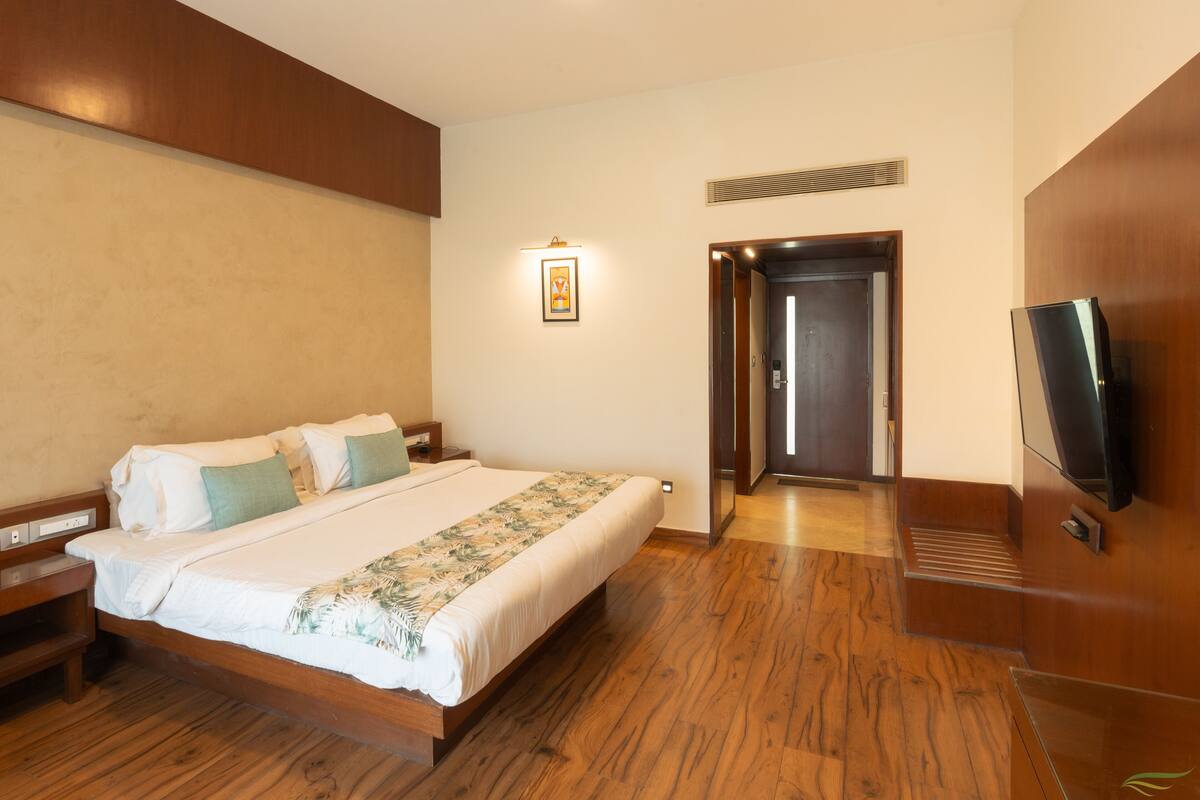 Una habitación de hotel con una cama de madera, un televisor montado en la pared y una puerta que da a otra habitación.