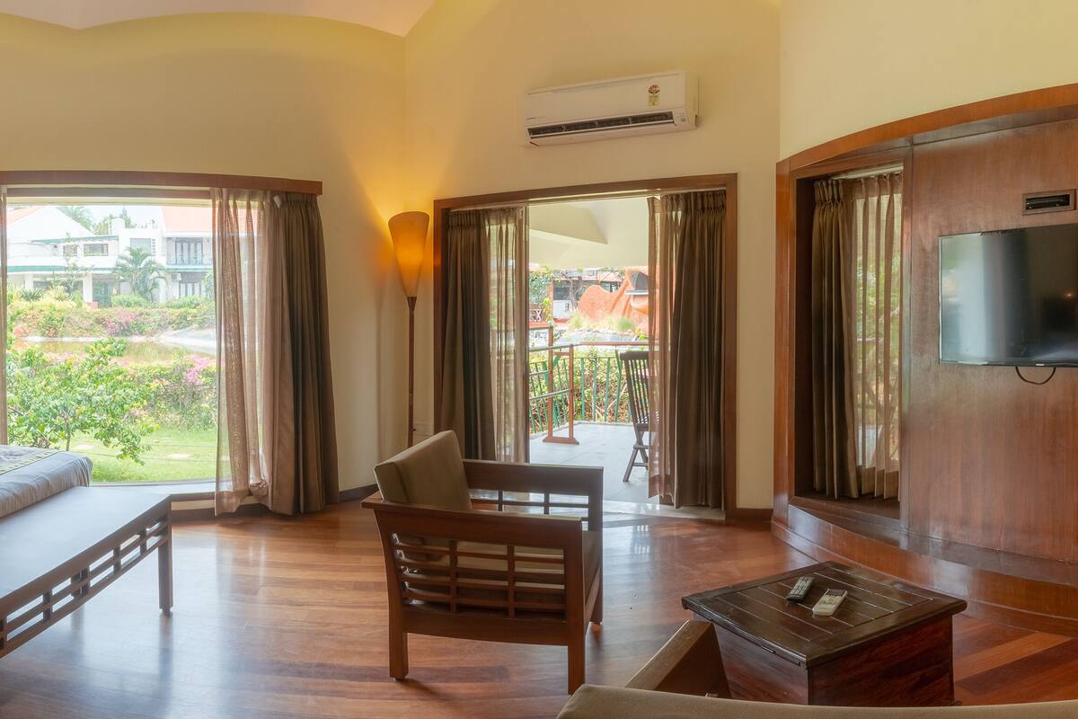 Habitación de hotel con una cama grande, un escritorio de madera, una silla, un televisor y un balcón con vistas al jardín.