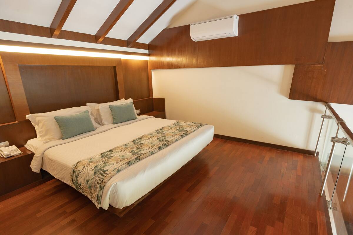 Habitación de hotel con piso de madera, cama con colcha estampada, mesita de noche con teléfono y aire acondicionado instalado en la pared.