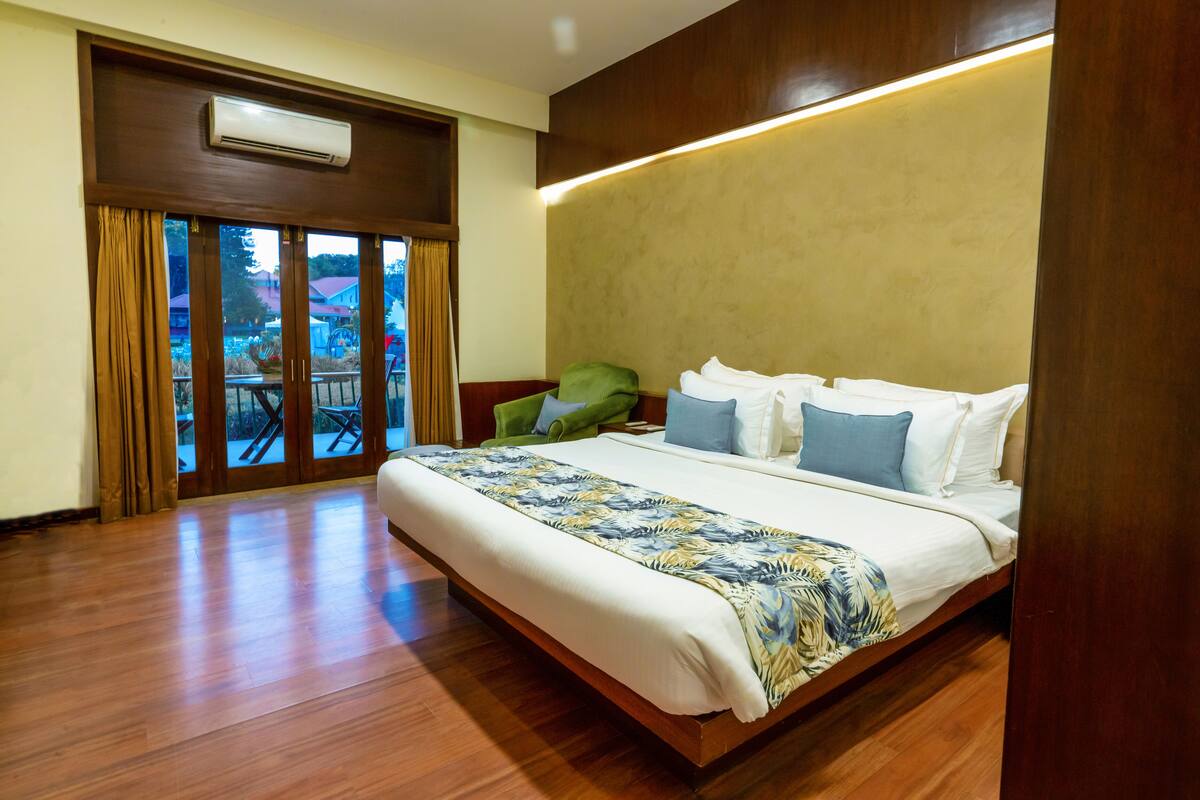 Habitación de hotel con una cama grande, suelo de madera, balcón con vistas y aire acondicionado instalado en el techo.
