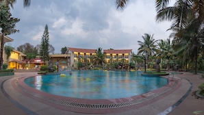 Zona de piscina de un resort con una gran piscina, palmeras y un edificio con varios balcones.