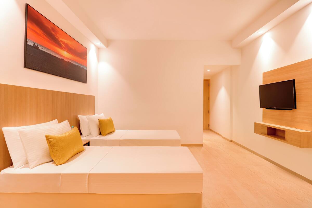 A modern hotel room with a large bed, a smaller sofa, a mounted TV, and a painting on the wall.