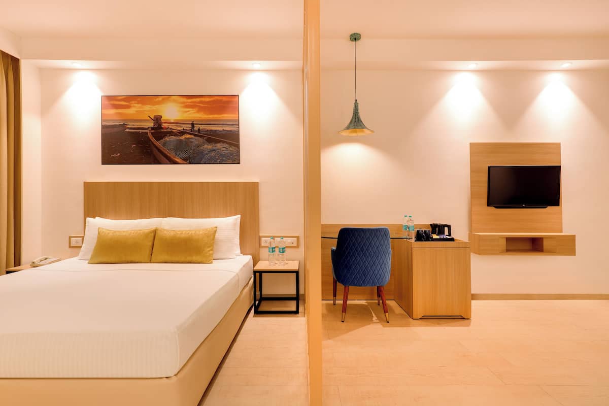 A hotel room with a bed, a desk, a chair, a TV, and a painting of a sunset.