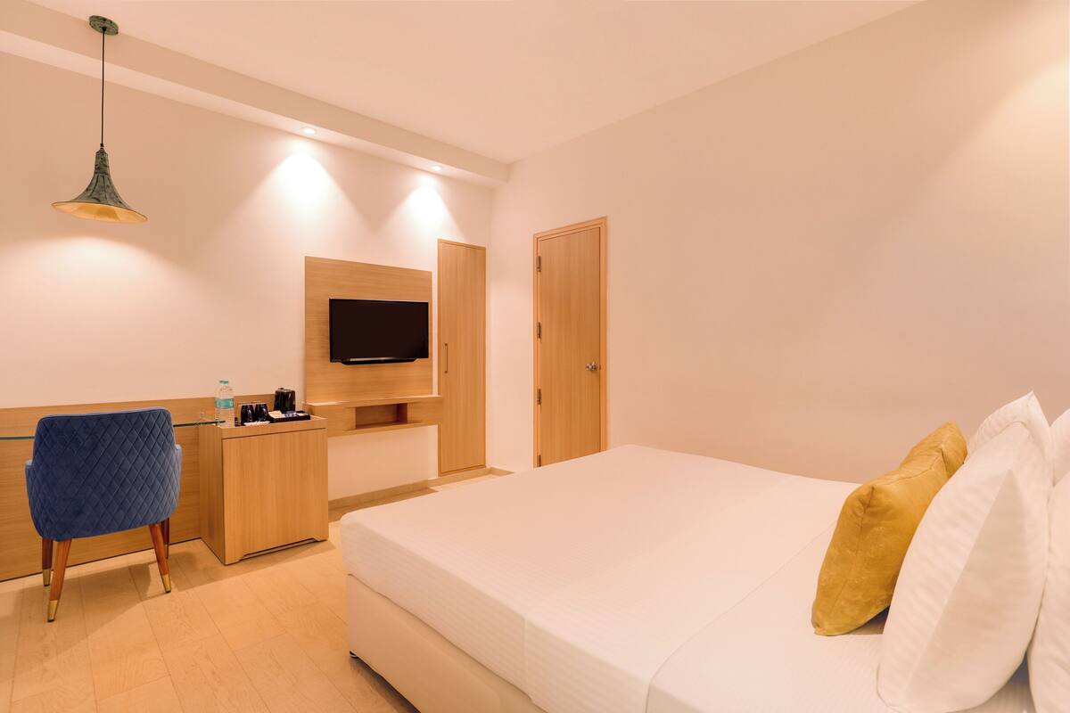 A hotel room with a bed, a desk, a chair, a TV, and a wardrobe.