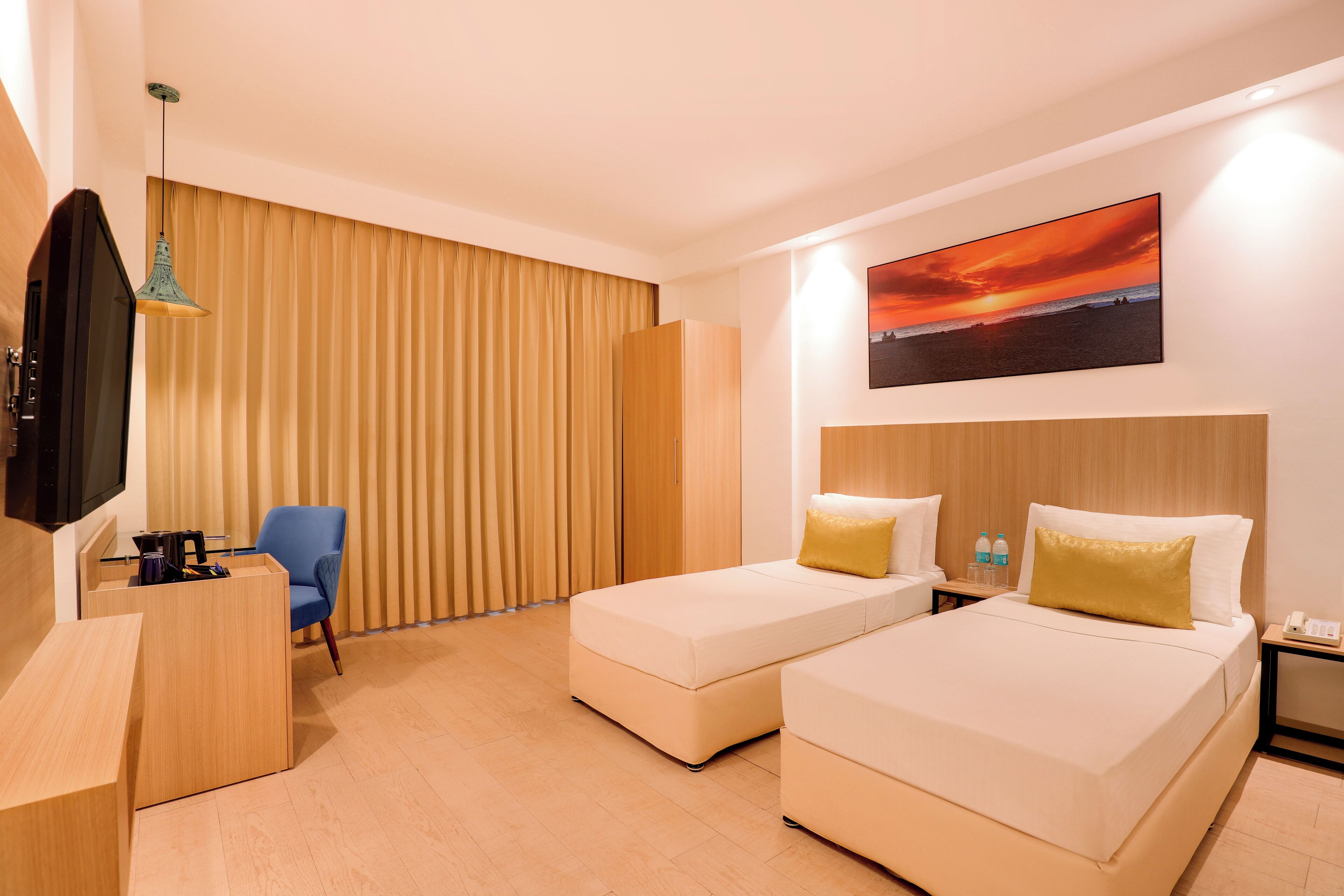Habitación de hotel con dos camas, un escritorio, una silla, un televisor y un cuadro de un atardecer.