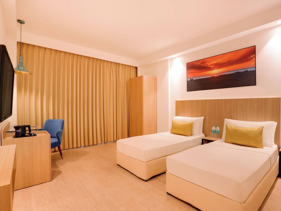 Habitación de hotel con dos camas, un escritorio, una silla, un televisor y un cuadro de un atardecer.