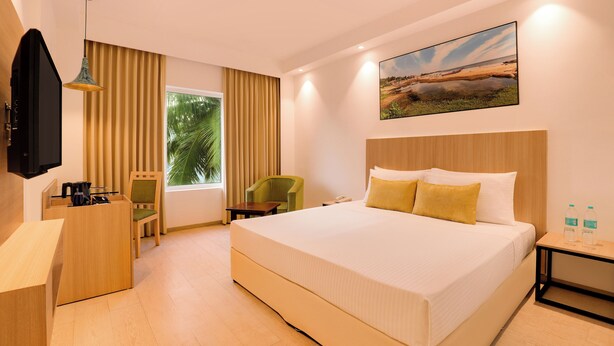 Habitación de hotel con una cama grande, un escritorio, una silla, un televisor y una ventana con cortinas.