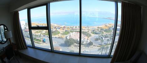 A room with a large curved window offering a view of a coastal area, including a beach and a road with vehicles.