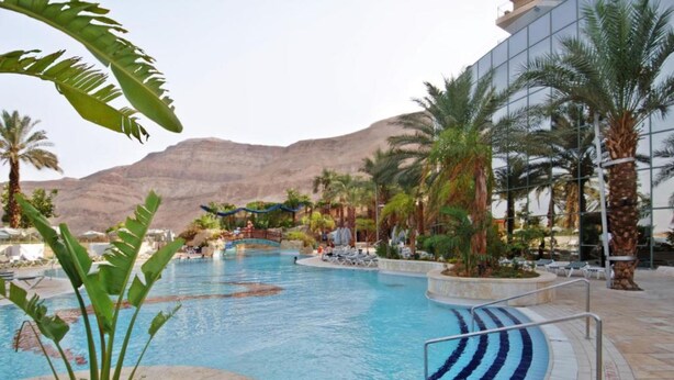 A pool area with lounge chairs and palm trees, surrounded by a modern building.