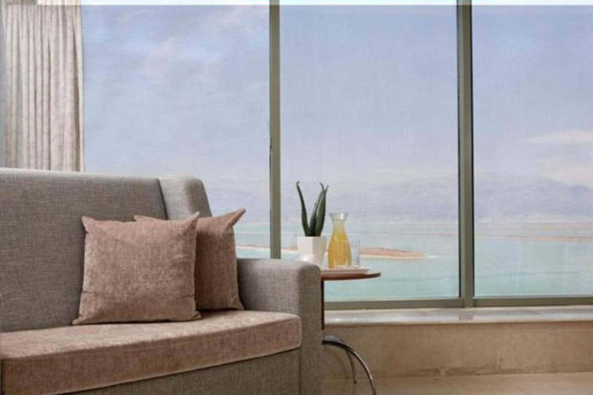 Een moderne woonkamer met een grijze bank, een klein bijzettafeltje en uitzicht op de zee door grote ramen.