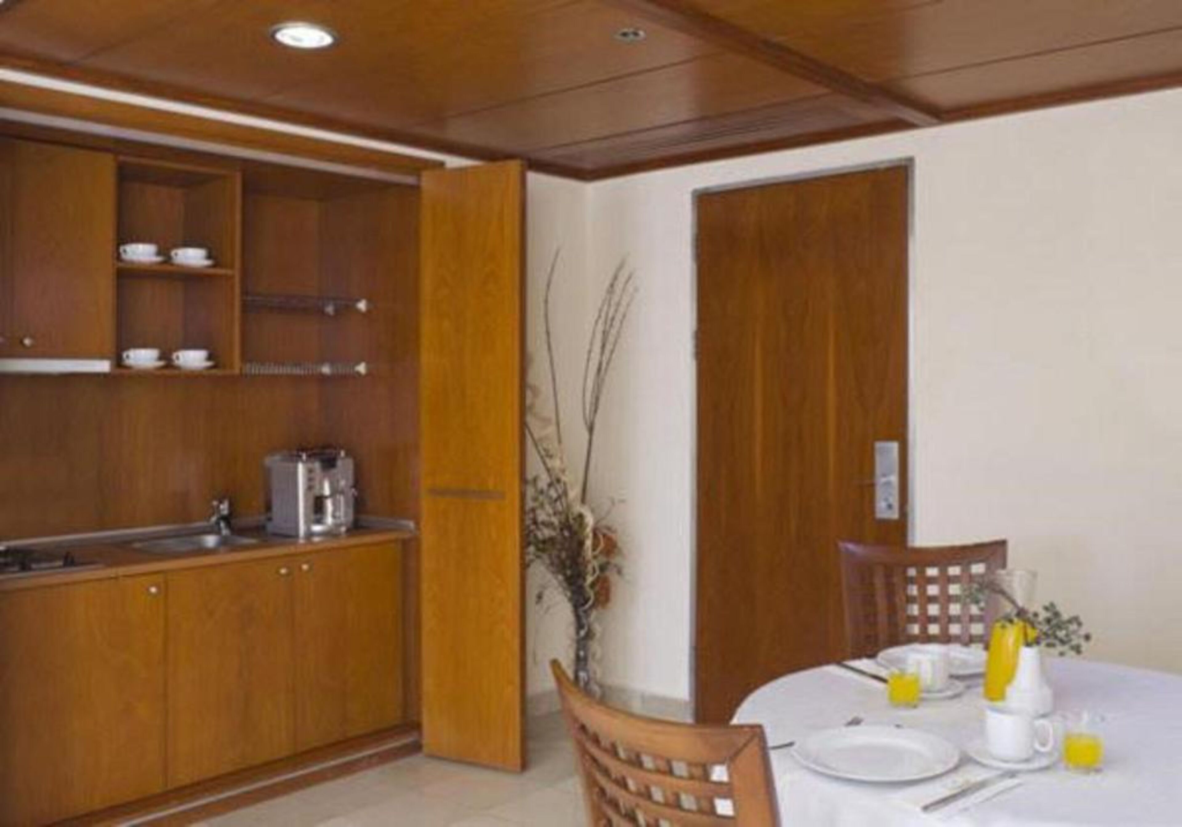 Un comedor con una mesa dispuesta para dos, una cafetera y un armario con tazas.