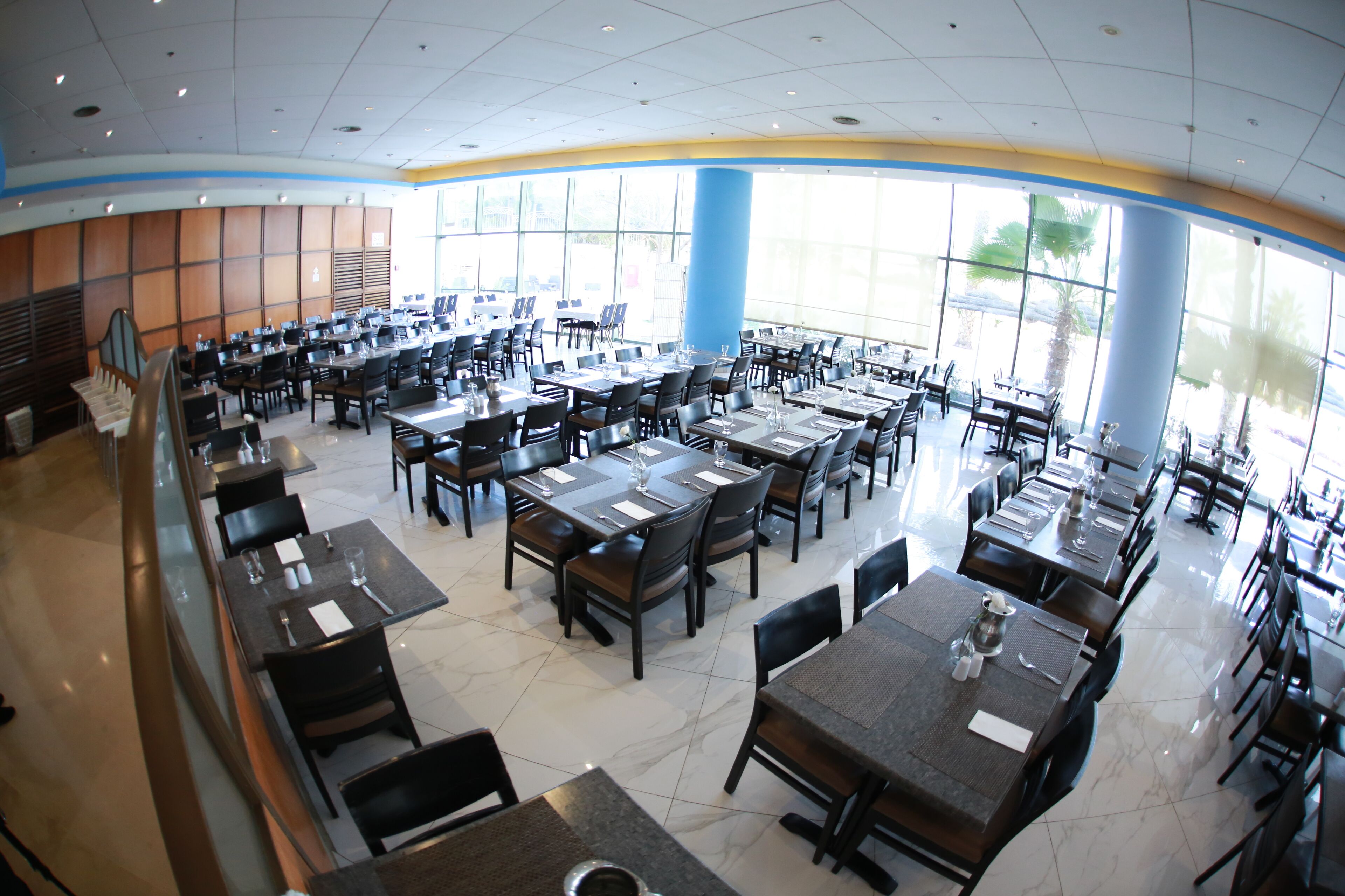 A spacious dining area with multiple tables and chairs, large windows, and a clean, modern design.