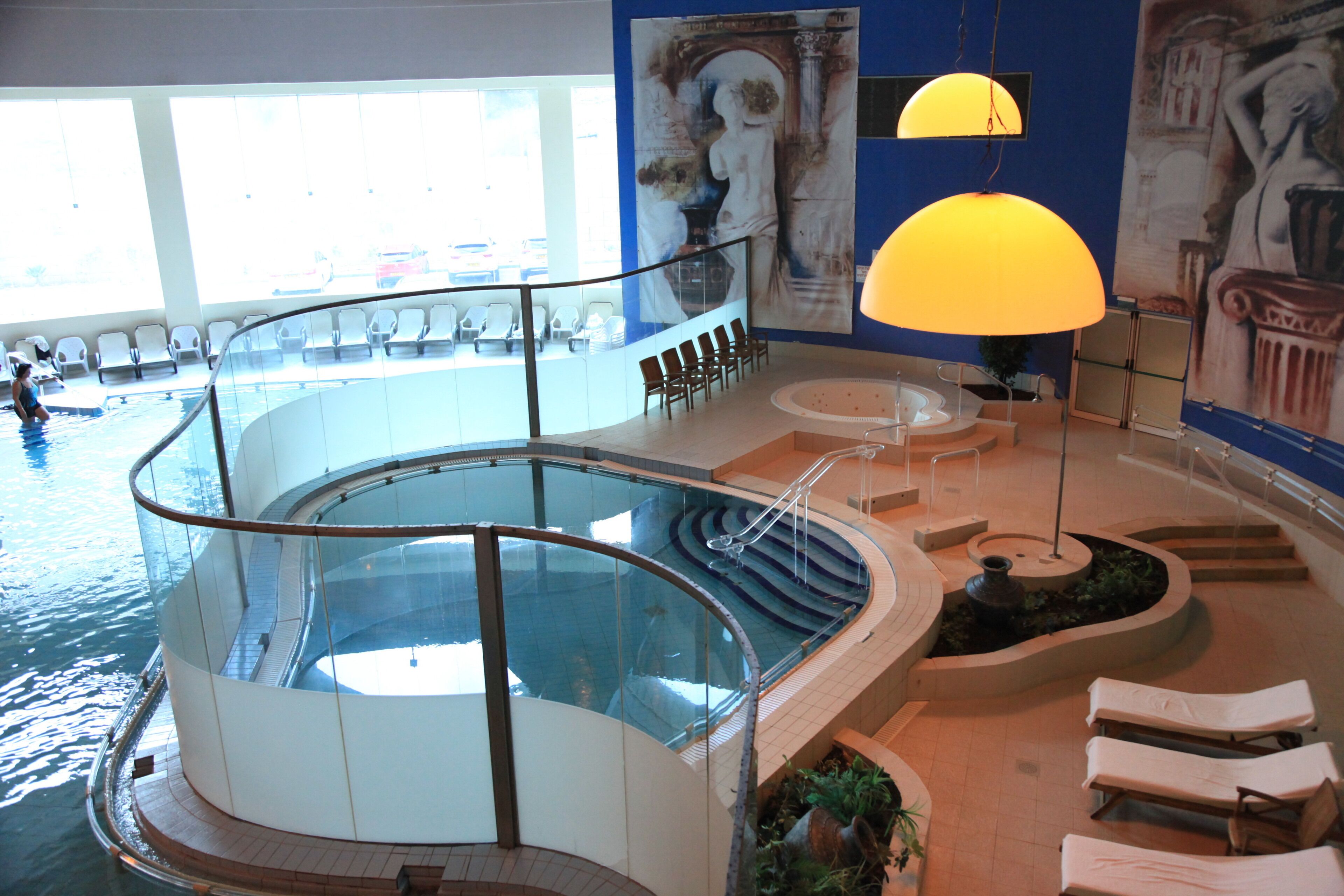 Ein Hallenbad mit Glasbrüstung, Liegestühlen und einer Sonnenbank.