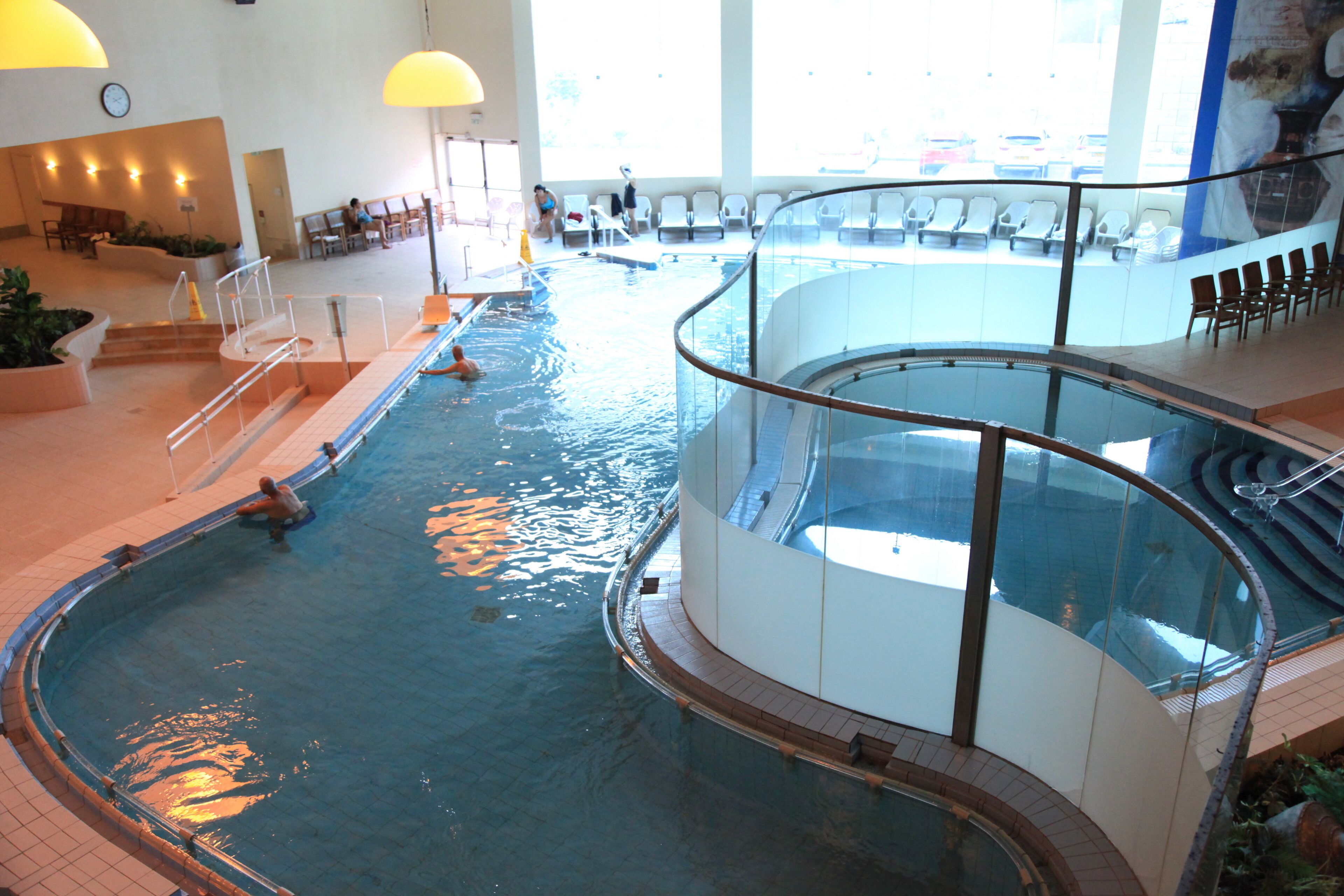 Una piscina interior con barandilla de cristal, zona de estar y vistas al exterior.