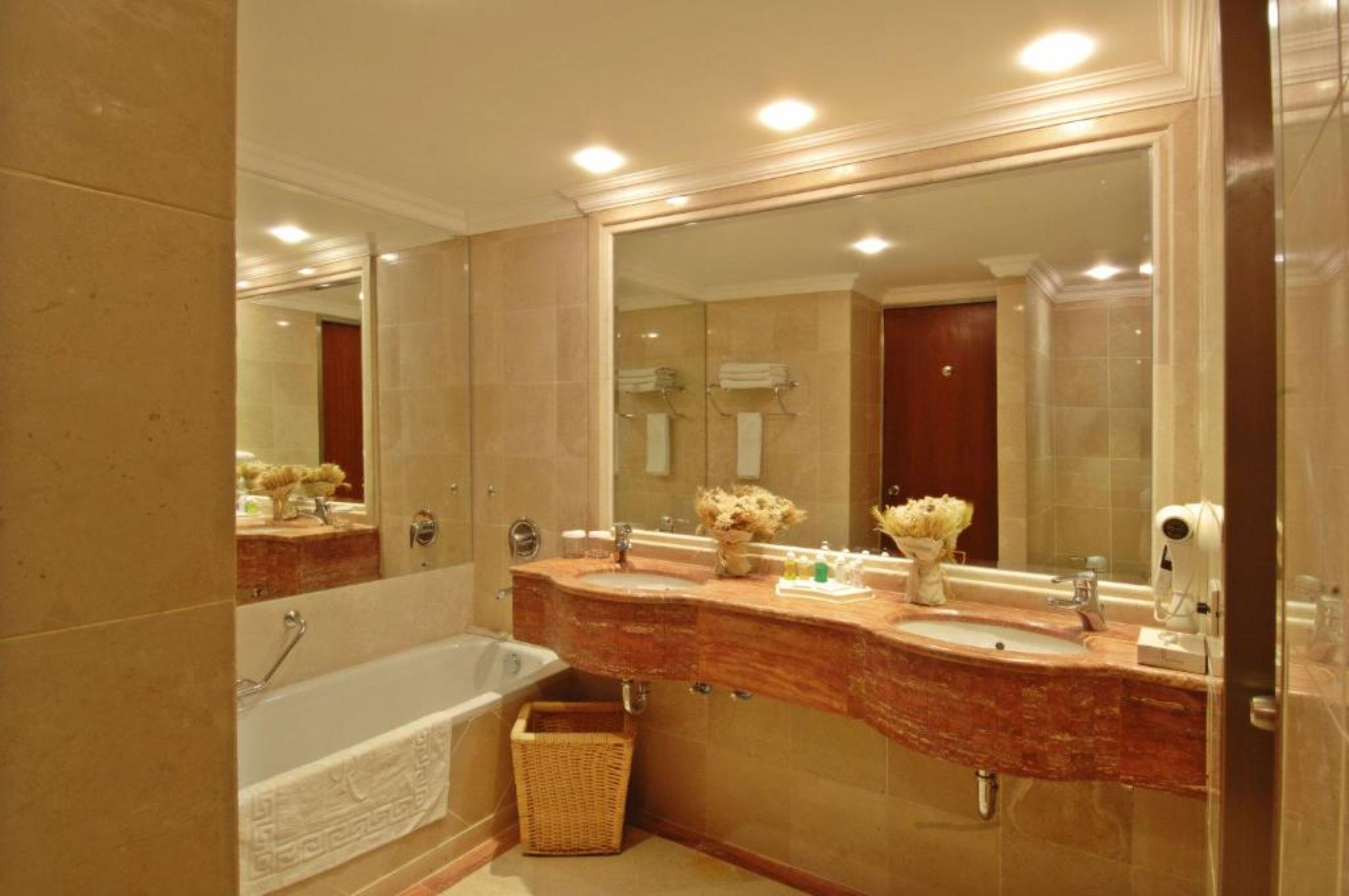 Un baño con un espejo grande, dos lavamanos, una bañera y una cesta de mimbre.