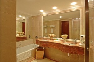 Un baño con un espejo grande, dos lavamanos, una bañera y una cesta de mimbre.