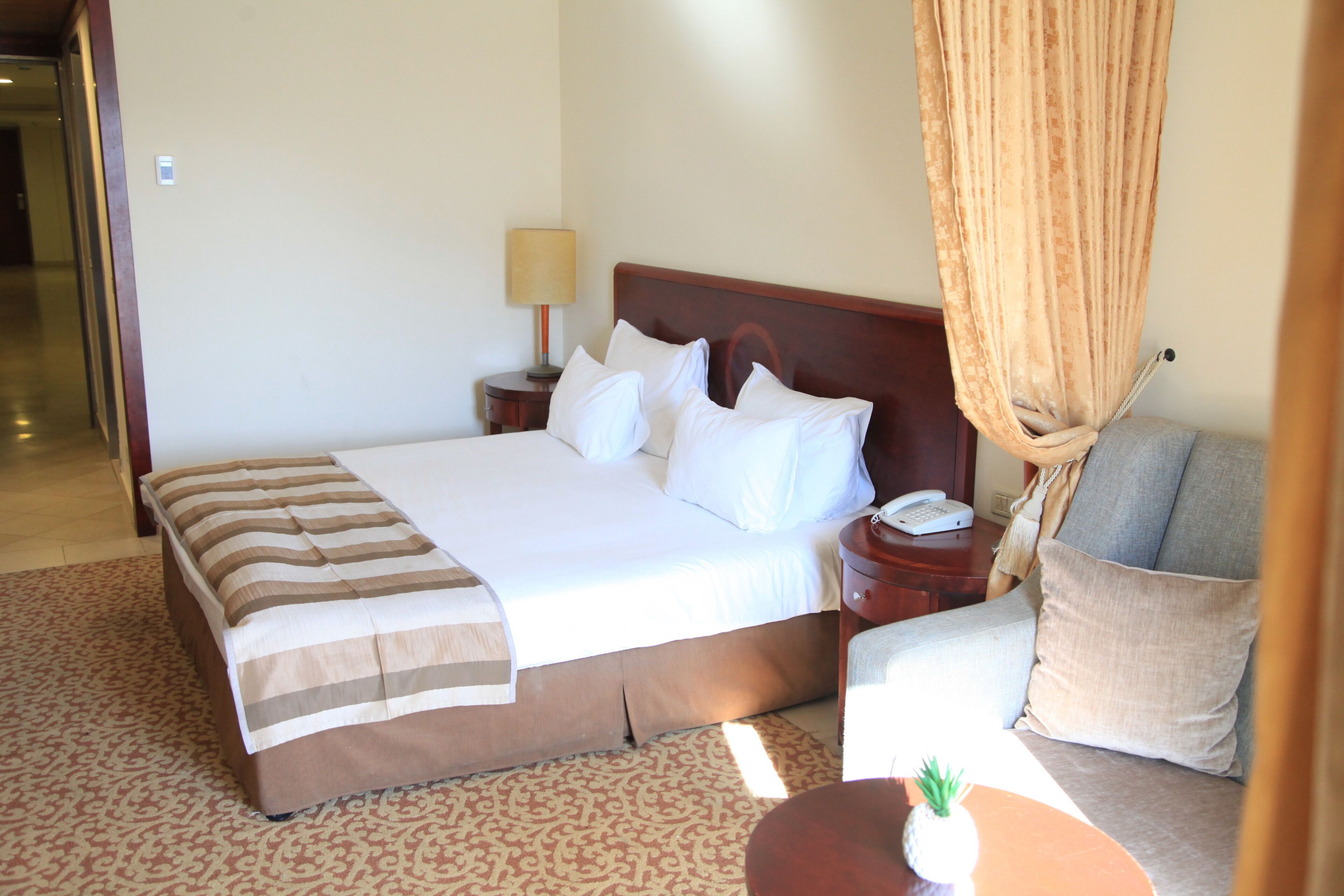 Una habitación de hotel con una cama, una mesita de noche con lámpara, un teléfono, un sofá y una pequeña mesa con una piña.