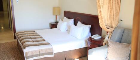 Una habitación de hotel con una cama, una mesita de noche con lámpara, un teléfono, un sofá y una pequeña mesa con una piña.