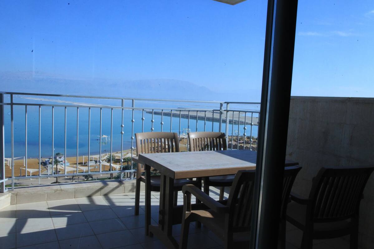 Een balkon met een tafel en stoelen, met uitzicht op een strand en de zee.