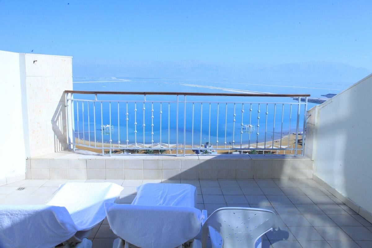 Een balkon met uitzicht op zee, een witte balustrade en twee witte loungestoelen.