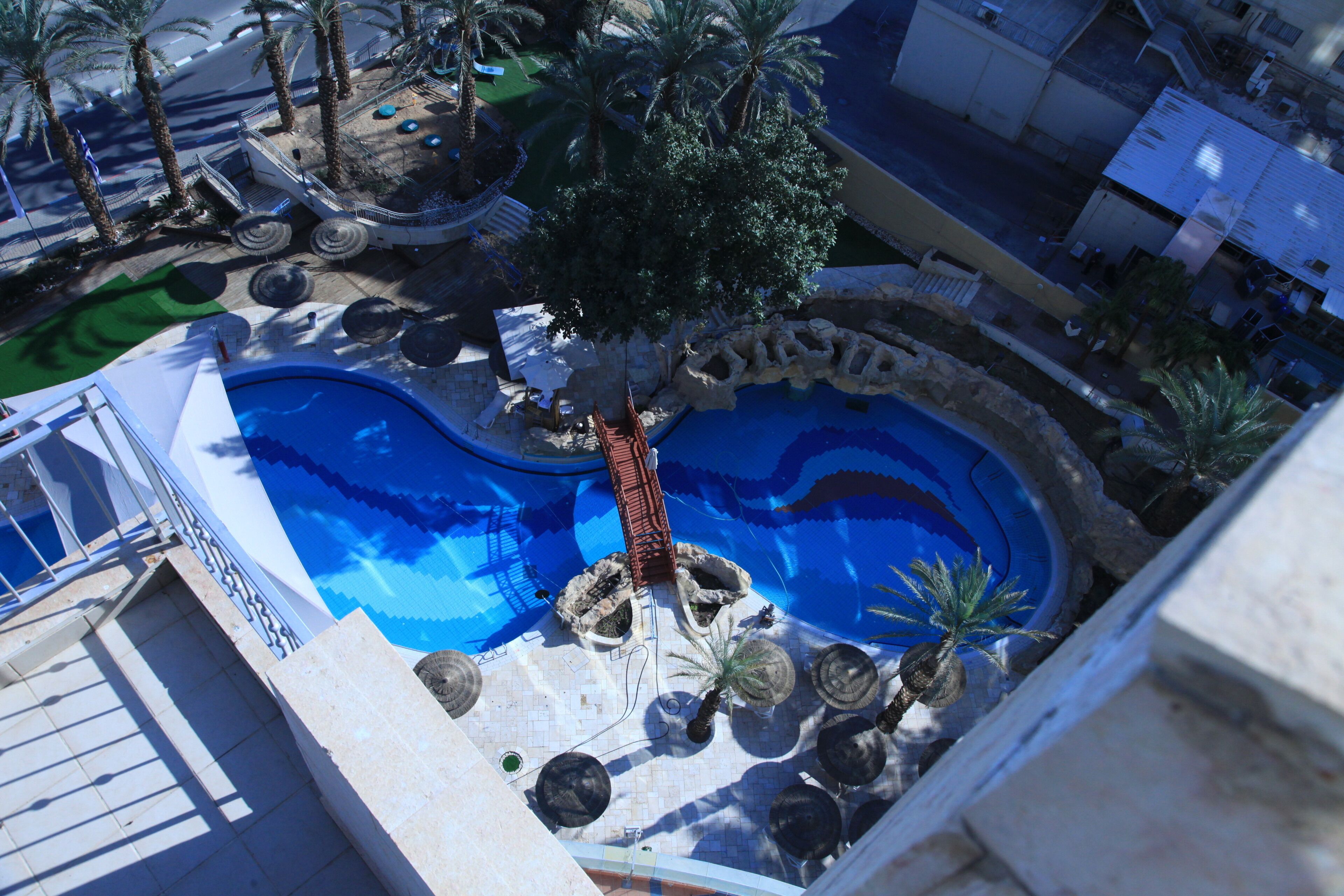 Luftaufnahme eines Swimmingpools mit umliegenden Palmen und einem kleinen Wasserfall.