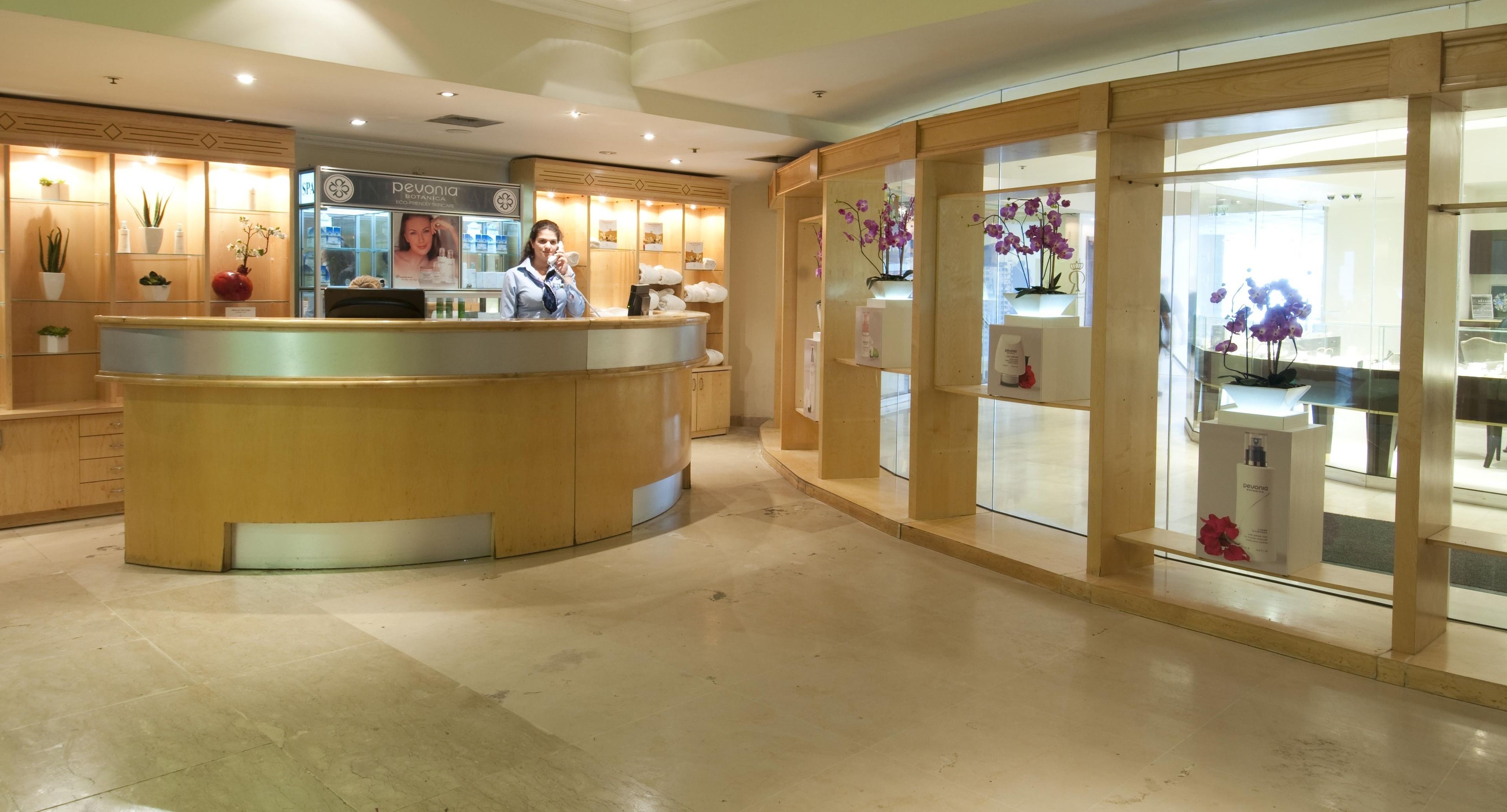 Ein Hotel-Empfangsbereich mit einem Holzbüro, einer Theke mit einer Glasvitrine und einem großen Fenster, das Orchideen zeigt.