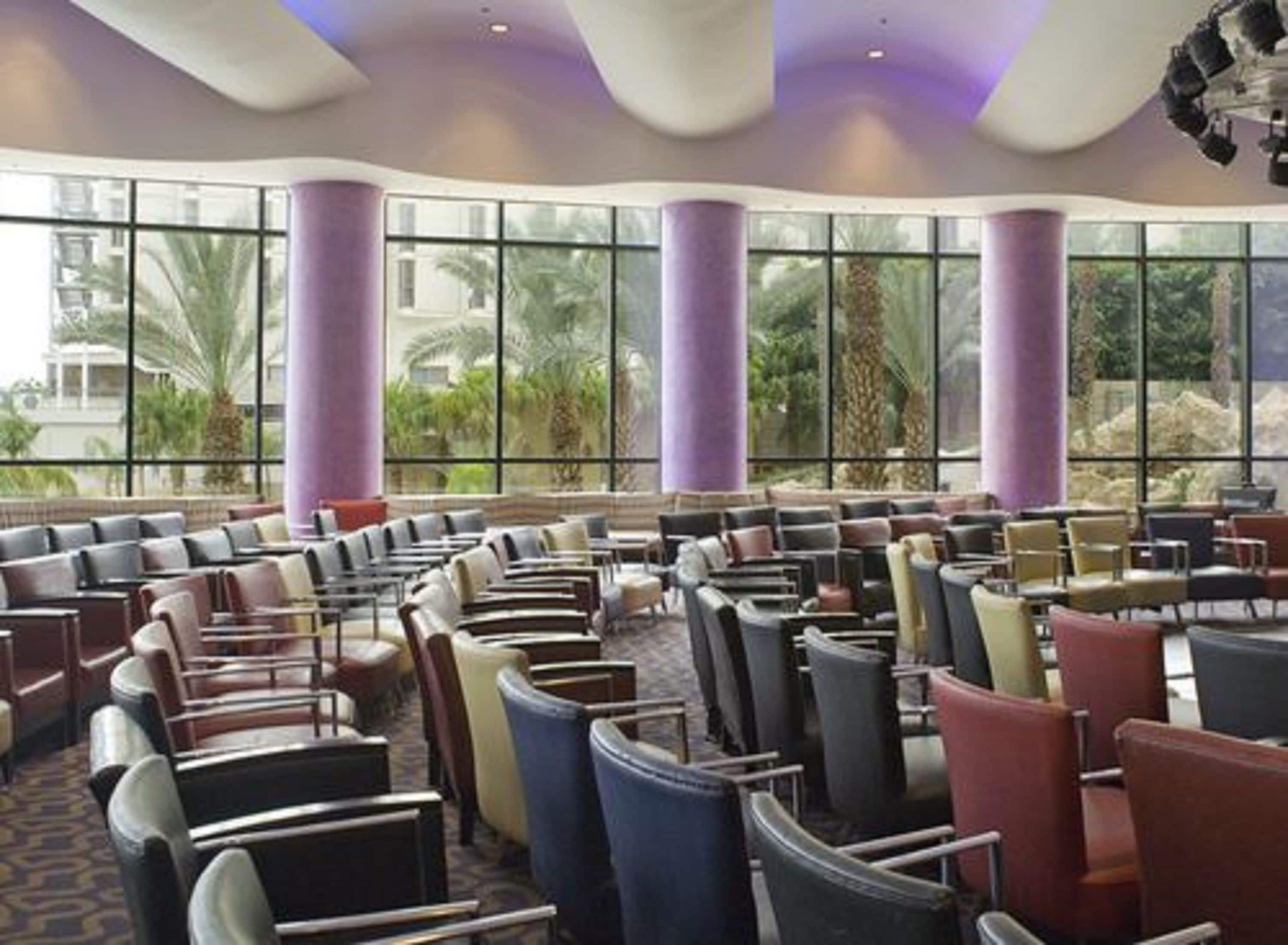A spacious indoor area with rows of chairs and tables, large windows, and purple pillars.