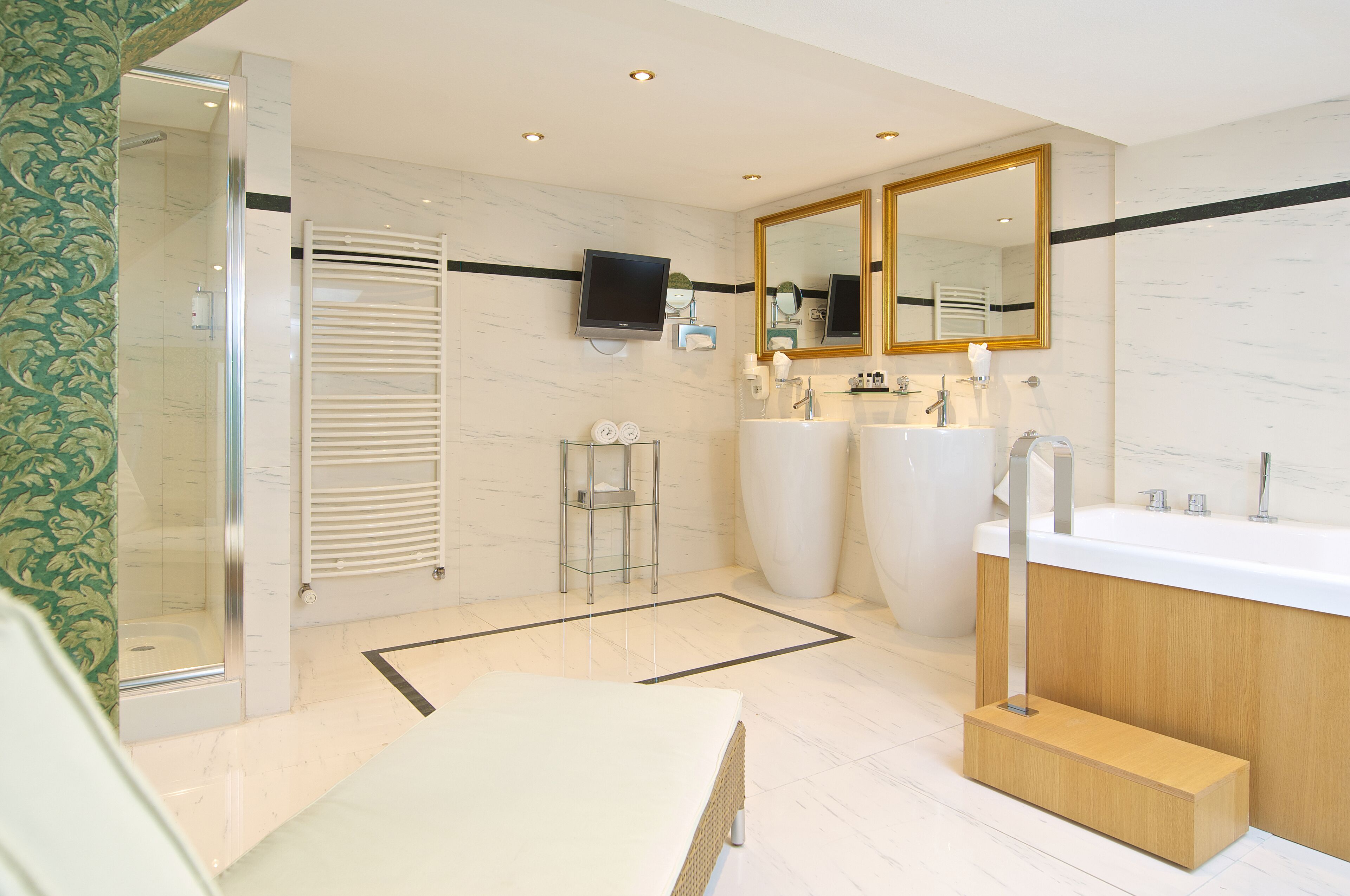 A modern bathroom with a large mirror, two sinks, a shower, and a television.