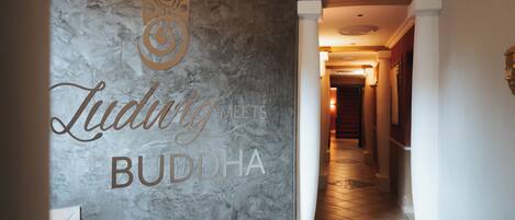 A hallway with a marble wall displaying the text "Ludwig Meets Buddha" and a staircase leading to an upper level.