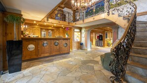 A grand lobby with a stone floor, wooden paneling, a chandelier, and a staircase with ornate metal railings. - Alpin & Wellness Resort Hotel Ludwig Royal  (Oberstaufen)
