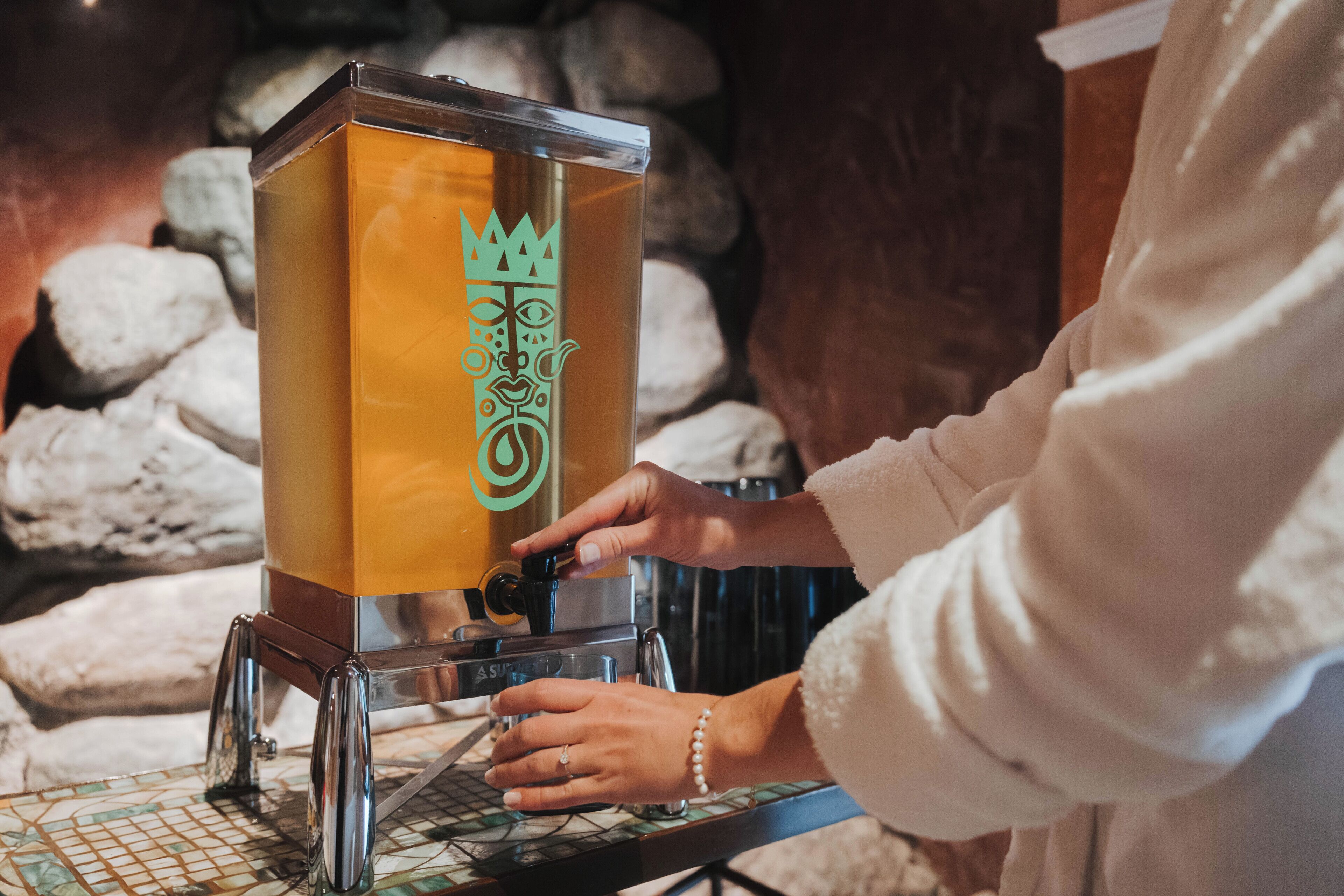A person operating a coffee machine with a decorative design, placed on a tiled surface with a stone background.
