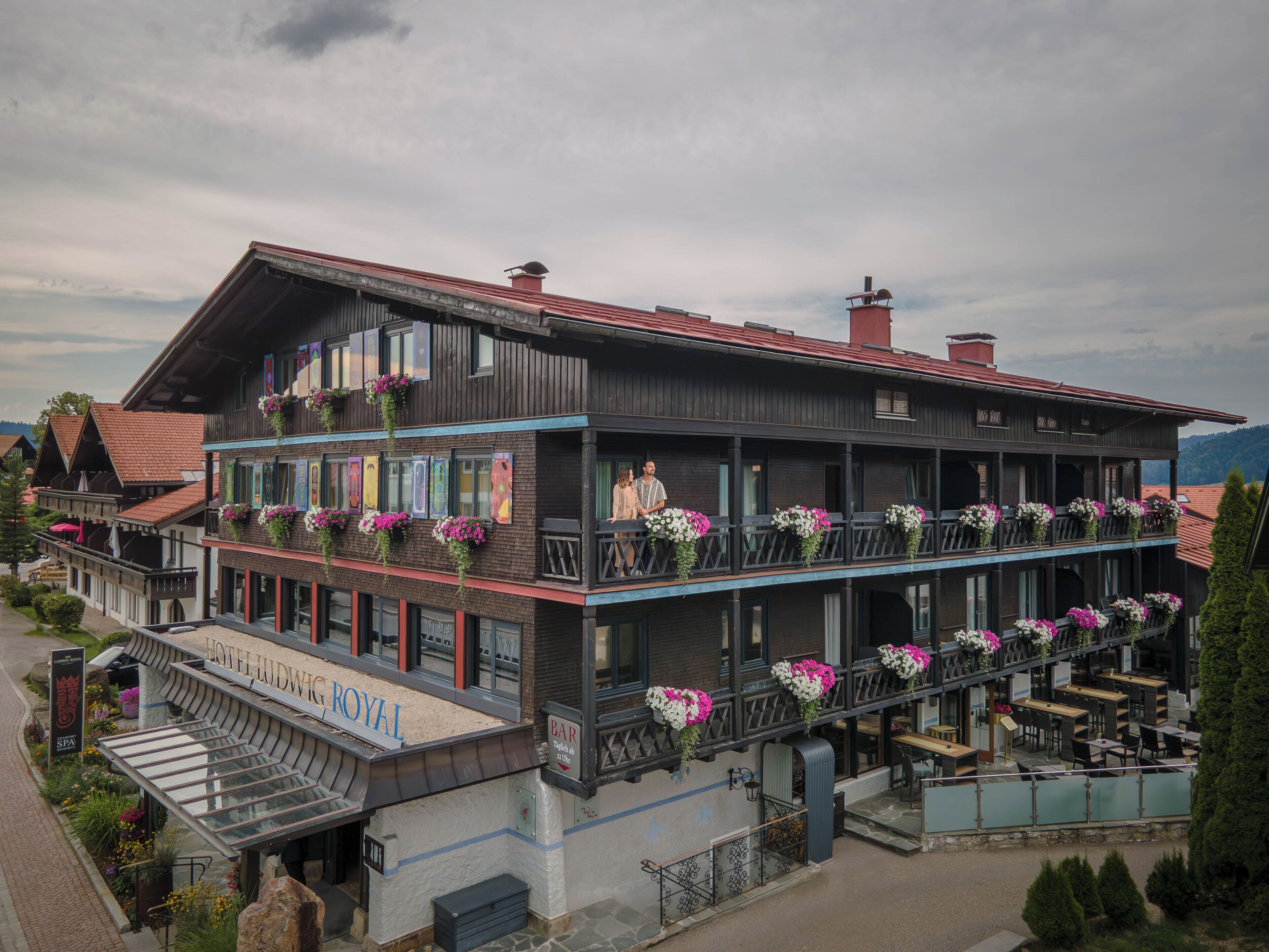 A hotel with a balcony, outdoor seating, and flower arrangements.