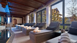 A sunlit spa area with wicker loungers, towels, and a view of a building with balconies. - Alpin & Wellness Resort Hotel Ludwig Royal  (Oberstaufen)
