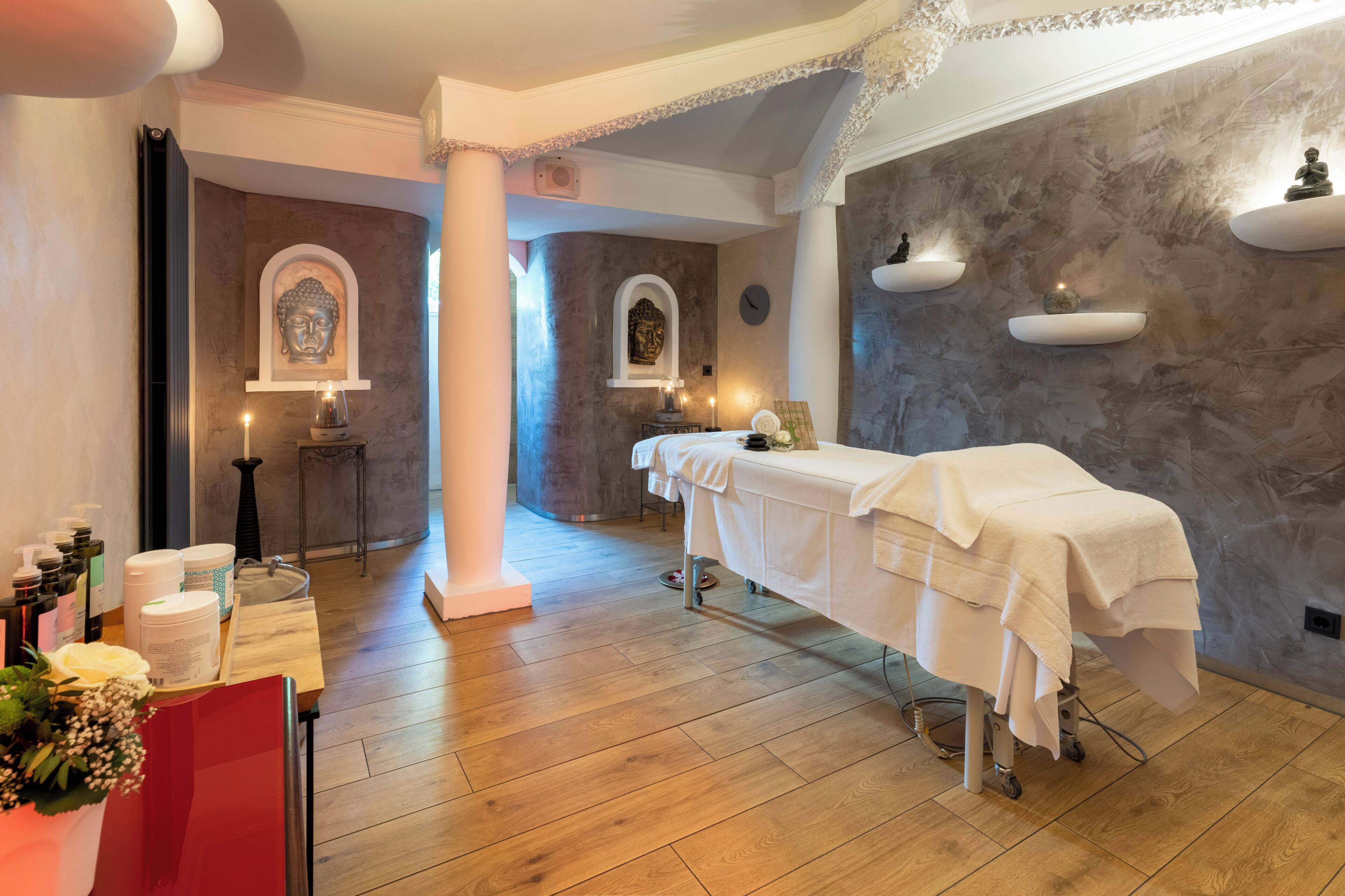 Un cuarto de spa con una camilla de masaje, velas y estatuas en estantes.
