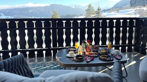 A balcony with a table set for breakfast, overlooking a snowy mountain landscape. - Alpin & Wellness Resort Hotel Ludwig Royal  (Oberstaufen)