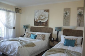A hotel room with two beds, a large floral artwork on the wall, and a window with sheer curtains. - Tariman INN (Umhlanga)