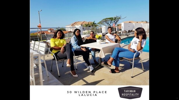 A group of people seated at a table with a pool in the background. - Tariman INN (Umhlanga)