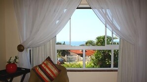 A room with a view of the sea, a chair, a small table with a vase, and sheer curtains. - Tariman INN (Umhlanga)