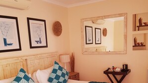 A neatly made bed with white and teal pillows, a teal throw blanket, and a wooden headboard. There are framed pictures on the wall, a mirror, and a small table with a lamp and decorative items. - Tariman INN (Umhlanga)