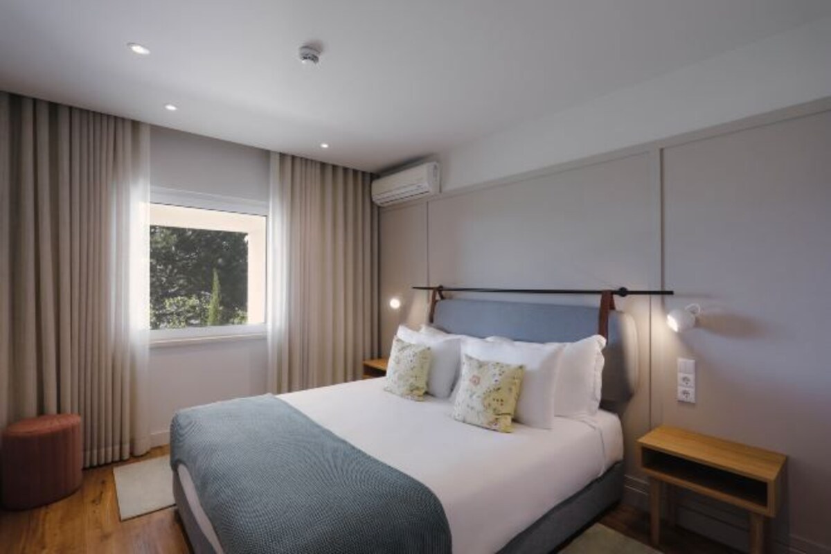 Un dormitorio moderno con una cama grande, una mesita de noche y un ventanal con cortinas.