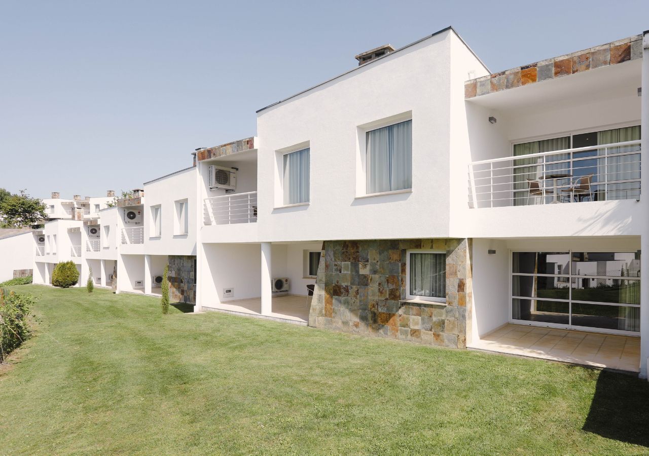 Un immeuble résidentiel moderne à plusieurs étages, doté de balcons, d’une façade en pierre et d’une pelouse bien entretenue.