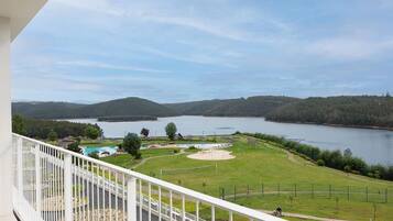 Un balcón con vistas a un lago, zonas verdes y un parque infantil.