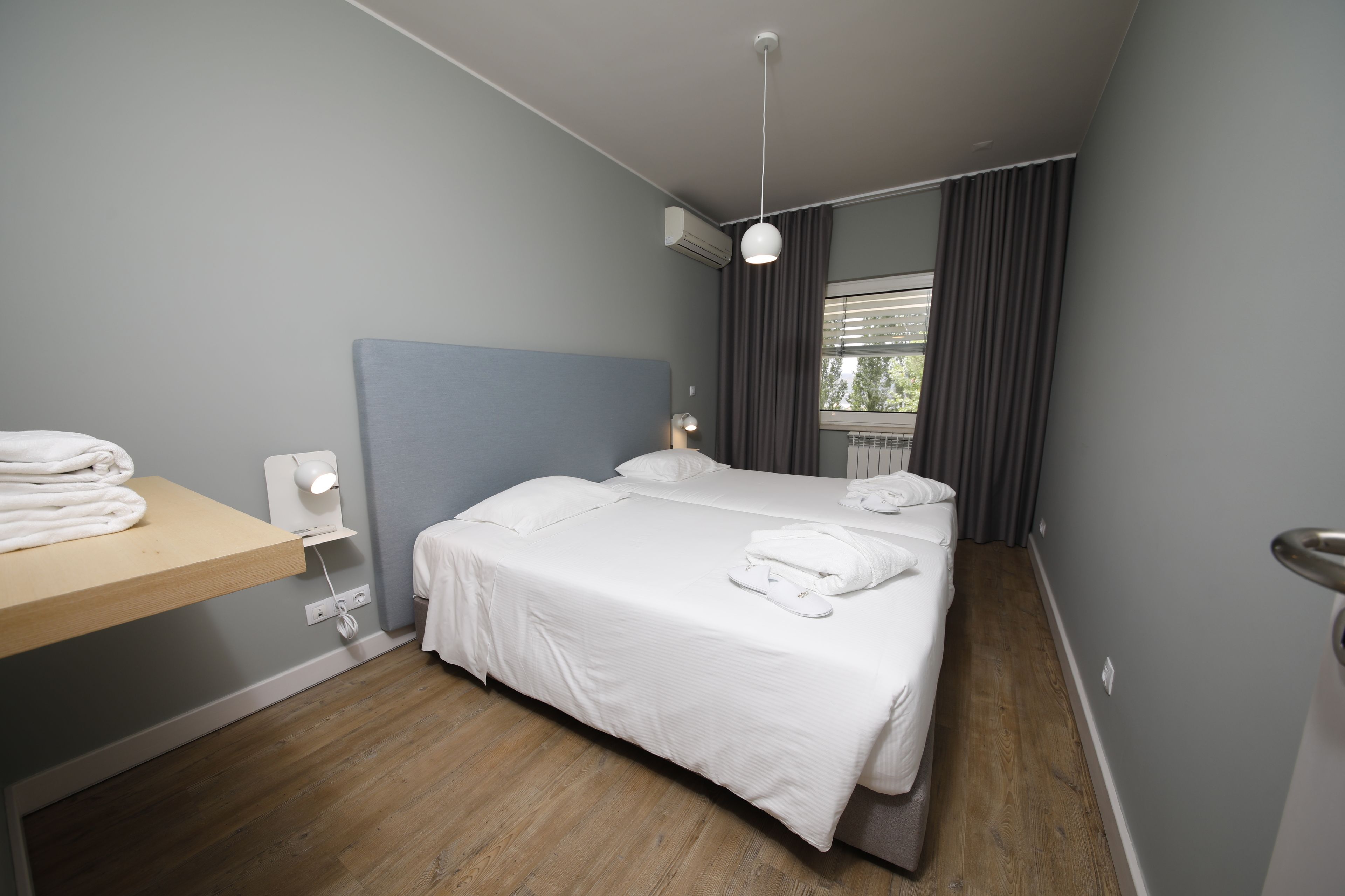 Habitació d'hotel amb un llit, una taula de nit amb tovalloles, aire condicionat fixat a la paret i una finestra amb cortines.