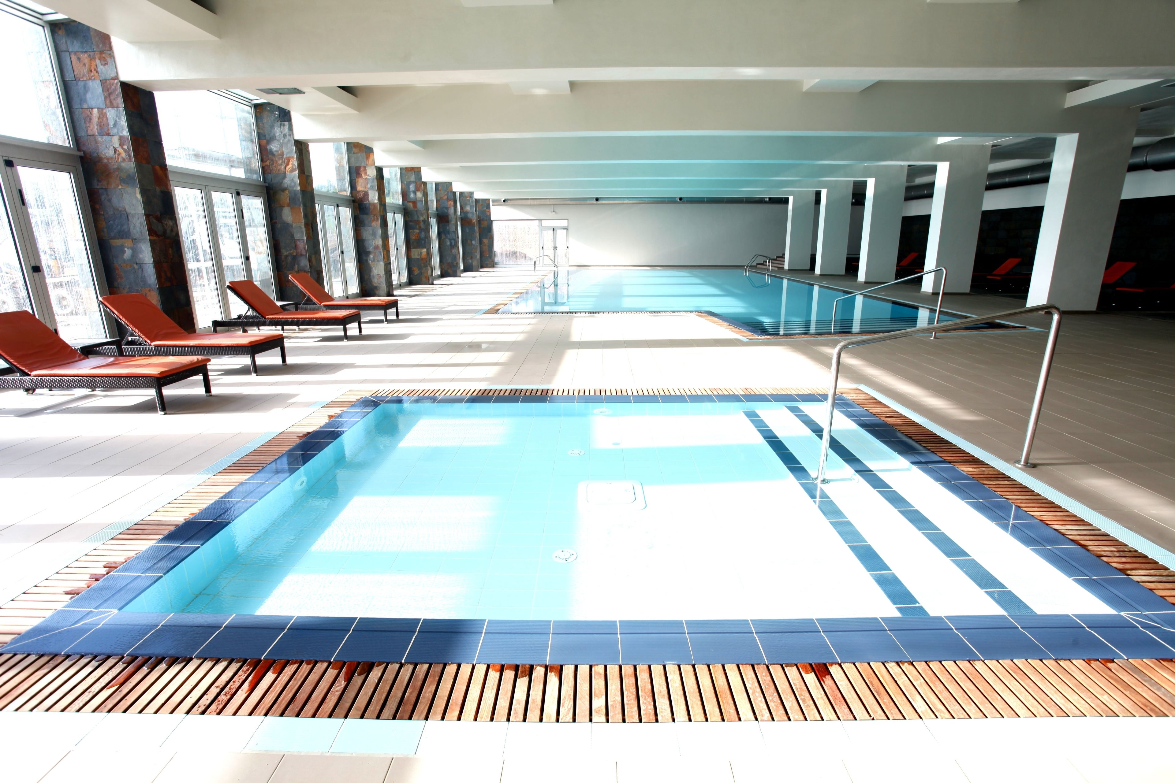 Uma grande piscina interior com áreas ensolaradas, espreguiçadeiras e chão revestido de azulejos.