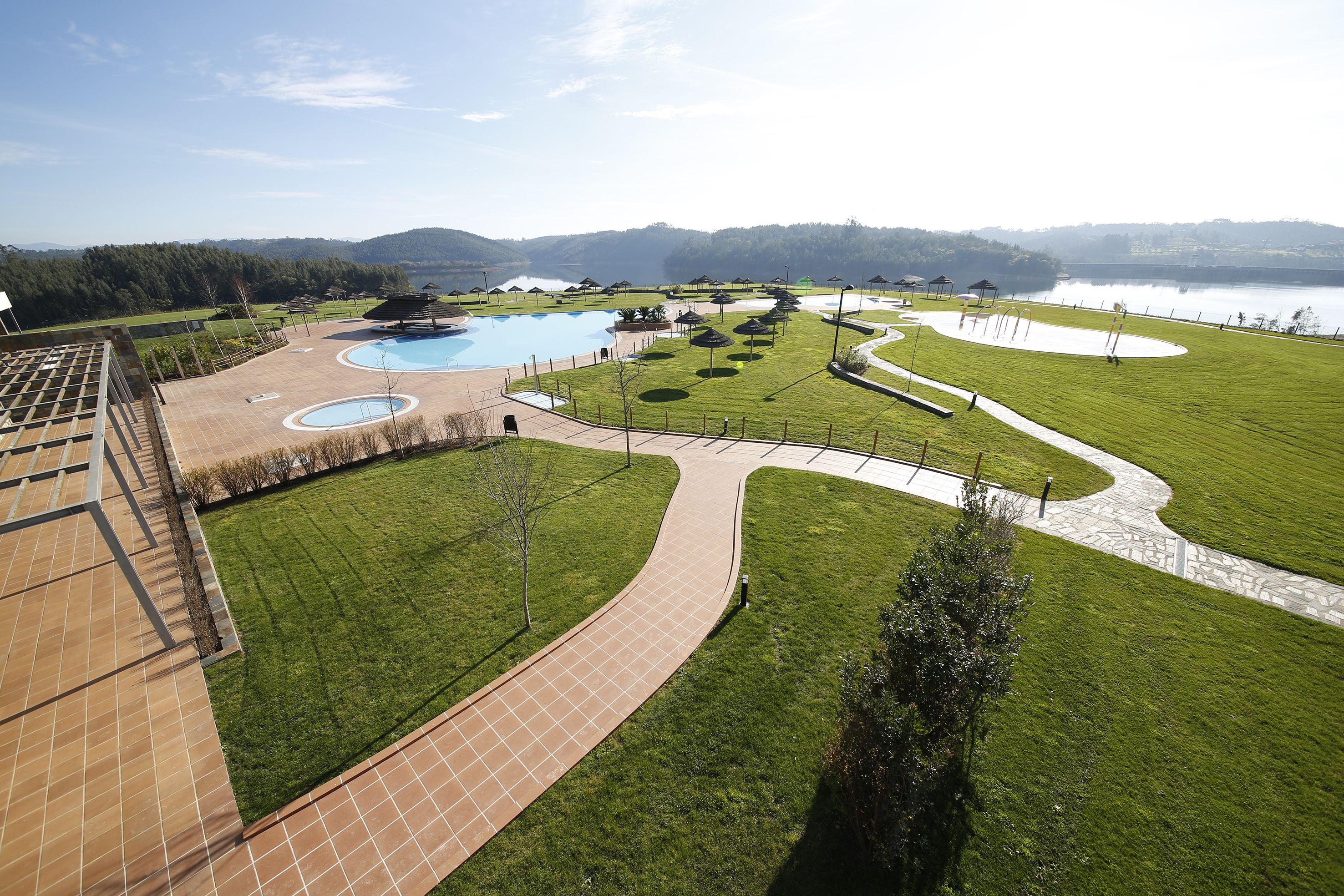 A resort with a swimming pool, walking paths, and a view of a lake and mountains.