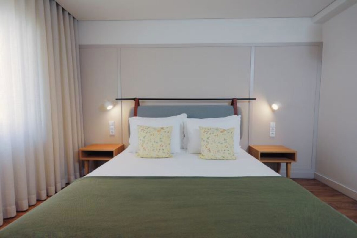 Una habitación de hotel con una cama grande, dos mesitas de noche y un cabecero con iluminación integrada.