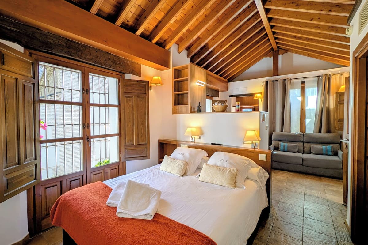 Un dormitorio con una cama grande, vigas de madera en el techo, un sofá y una zona de cocina.